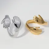 Set de dos anillos unisex, uno dorado y otro plateado, con diseño de manos abrazándose.