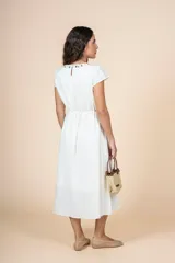 Vestido midi de color blanco con silueta recta, escote redondo adornado con apliques metálicos y mangas cortas. Incluye un lazo ajustable en la cintura para entallar la prenda.