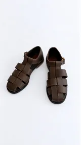 Sandalias cangrejeras de gamuza color marrón, con punta redonda, taco bajo, talonera cerrada y tira con hebilla metálica ajustable en el tobillo.
