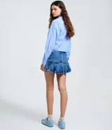 Short pollera de jean azul con diseño de cintura cruzada, doble abotonado y pliegues amplios en el ruedo. Confeccionado en algodón, combina la comodidad de un short con la estética de una minifalda.