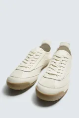 Zapatilla de estilo retro con cordones, confeccionada en una combinación de piezas de cuero sintético negro y detalles en blanco, con suela dentada de goma en tono caramelo.