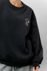 Buzo oversize de algodón frizado color beige, con cuello redondo, puños y cintura tejidos. Presenta un bordado pequeño de Snoopy en el frente.