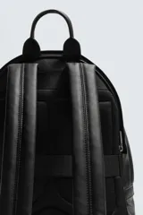 Mochila de diseño minimalista en color negro con acabado grabado. Cuenta con un compartimento principal con cierre de cremallera, un bolsillo frontal con cierre y un compartimento posterior acolchado para dispositivos electrónicos. Incluye asa de mano superior y dos asas de hombro ajustables.