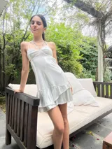 Vestido corto de tela satinada color plata, con diseño tipo corset en el top, breteles finos y falda con volados superpuestos.