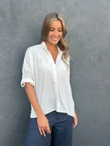Camisa blanca de corte holgado y asimétrico, con cuello camisero y cierre frontal de botones.