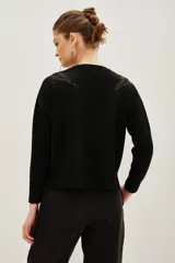 Sweater negro de punto con cuello redondo, manga larga y detalle de tachas metálicas en los hombros formando un diseño de rayo.