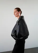 Parka oversize de cuero de piel de ovino color negro, con cuello embudo, solapas amplias y cierre oculto de cremallera y botones. Cuenta con manga larga con puños elásticos y dos bolsillos laterales.