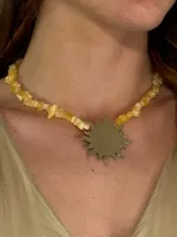 Collar corto de piedras irregulares color amarillo con dije metálico plateado en forma de sol.