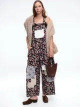 Mono de estilo jardinera con estampado floral y detalles de parches en diferentes texturas y patrones. Presenta un bolsillo frontal en color claro, tirantes ajustables con hebillas metálicas y piernas de corte recto y holgado.