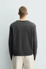 Camiseta de manga larga con corte relajado, confeccionada en algodón. Presenta un cuello redondo amplio con acabado irregular y detalle de botones frontales a tono.