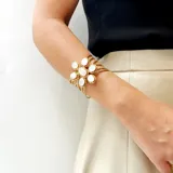 Pulsera artesanal de bronce con diseño de flor central compuesta por piedras blancas de forma ovalada. Presenta una estructura de múltiples hilos metálicos que forman un brazalete tipo cuff.