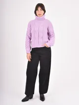 Polera de tejido de punto color lila, con cuello alto doblado y diseño de trenzas en el frente y las mangas. Presenta puños y ruedo acanalados.
