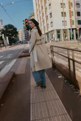 Trench largo de color negro con cuello de solapa, cierre frontal cruzado con botones y cinturón ajustable a tono. Presenta mangas largas con trabillas en los puños, bolsillos delanteros de vivo y abertura en la espalda.