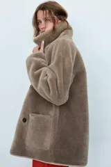 Abrigo reversible de corte recto con cuello solapa, manga larga y cierre frontal de doble botonadura. Presenta un diseño de efecto pelo en un lado y efecto piel en el reverso, con bolsillos de plastrón en el frente.
