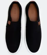 Championes tipo slip on marca Viko, de color negro con suela de goma blanca. Presenta un diseño minimalista sin cordones con paneles elásticos laterales y un pequeño detalle de etiqueta en color marrón.