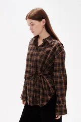 Camisa de poliéster con estampado a cuadros, cuello camisero, cierre frontal con botones y detalle de lazo ajustable en la cintura.