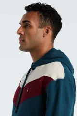 Hoodie de corte regular con diseño de bloques de color en azul petróleo, bordó y beige. Presenta capucha con cordones ajustables, bolsillo tipo canguro frontal y puños y ruedo acanalados. Incluye un pequeño logo bordado en el pecho.