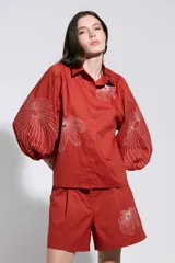 Camisa roja con bordados florales blancos, cuello camisero, cierre frontal oculto y mangas largas abullonadas.