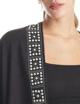 Ruana negra de tejido soft con terminación de flecos en el ruedo. Presenta una guarda frontal decorada con perlas y detalles brillantes.