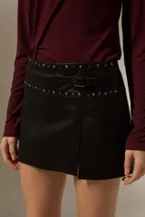 Minifalda de cuero sintético color negro, con diseño de tajo frontal y detalle de cinturón integrado con tachas metálicas en la cintura.