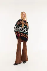 Sweater de punto oversize con diseño de intarsia geométrica y letras en tonos marrón, amarillo y rosado. Presenta cuello redondo, mangas largas y puños acanalados.