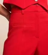 Bermuda femenina de sastrería color rojo, confeccionada en tejido de crepé. Presenta trabillas en la cintura, cierre delantero y bolsillos falsos.