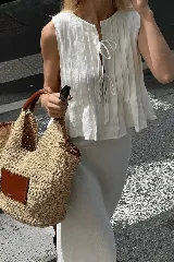 Conjunto de top y falda color crema, confeccionado en lino. El top es sin mangas, con detalle de lazos en el escote y volados en el ruedo. La falda es larga y de corte recto.