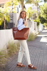 Bolso tote de cuero color tostado con costuras blancas a la vista en los laterales y doble asa de hombro.