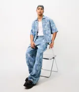 Camisa de jean de algodón con textura jacquard y diseño geométrico, de corte boxy, cuello con solapa, manga corta y cierre frontal con cremallera.