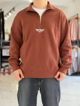 Buzo de felpa color beige con cuello alto, cierre frontal parcial, mangas largas y puños elastizados. Presenta un pequeño estampado en el pecho con la leyenda 'Top Style' y texto secundario.