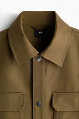 Sobrecamisa boxy de algodón, color verde militar, con cuello inglés, tapeta con botones a presión y bolsillos superiores con solapa.