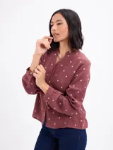 Blusa de algodón color bordó con estampado de lunares claros, cuello mao, cierre frontal con botones y mangas largas.