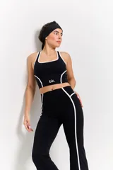 Conjunto deportivo compuesto por un top de escote redondo y calzas de tiro alto con diseño acampanado. Ambas piezas son de color negro con detalles de costuras blancas en contraste y logo estampado en el frente del top.