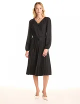 Vestido midi negro de satén, marca Sharagano. Presenta escote en V con aplique de guipur y lazo fino central. Mangas largas fluidas con puños fruncidos y hombros con leves frunces. La cintura tiene un lazo de ajuste que da paso a una falda de tablas plisadas.