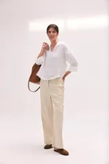 Pantalón de lino lavado color beige, de calce recto y diseño relajado. Presenta cintas de lino desflecadas aplicadas en los laterales con pespunte central, pretina con botón metálico, bolsillos delanteros y traseros.