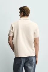 Polo de corte regular fit en tejido de algodón con estructura vertical color beige. Presenta cuello solapa, cierre frontal de botonadura y manga corta con rib.