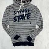 Canguro gris con rayas horizontales en tonos gris, rosa y blanco. Estampado frontal con la frase "Savage State" en letras negras. Tiene capucha con cordones blancos, bolsillo tipo canguro y puños negros.