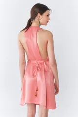 Vestido corto color durazno, con escote halter, espalda descubierta, volado asimétrico en el ruedo y lazo para ajustar en la cintura.