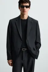Blazer de corte regular fit confeccionado en tejido con lana. Presenta cuello con solapas de muesca, cierre frontal de dos botones, manga larga con puños abotonados, bolsillo de vivo en el pecho y bolsillos con solapa en la cadera.