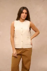 Chaleco de tejido de punto color crema, sin mangas, con cuello redondo y cierre frontal de botones dorados. Cuenta con dos bolsillos frontales aplicados con detalles de botones dorados.