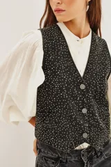 Chaleco de algodón negro con diseño de chaleco de vestir, cuello en V y cierre frontal con botones. La tela está completamente adornada con pequeños apliques brillantes que simulan un efecto de estrellas o puntos de luz.