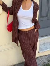 Conjunto de dos piezas compuesto por un blazer y un pantalón de corte sastrero, confeccionados en tela de algodón con estampado de rayas verticales blancas sobre fondo gris. El blazer presenta solapas clásicas y cierre frontal, mientras que el pantalón es de tiro medio y pierna recta.