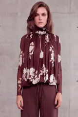 Camisa bordó de manga larga en tejido translúcido, con estampado floral en tonos claros y un pañuelo o echarpe integrado al cuello que cae sobre el frente.