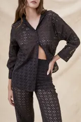 Camisa negra de algodón con bordado calado, corte oversize, cuello clásico, cierre frontal con botones y mangas largas con puños abotonados.