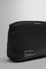 Neceser deportivo negro de tejido técnico con compartimento principal con cierre de cremallera, bolsillo interior, bolsillo frontal con cremallera y asa de mano.