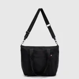 Tote bag de diseño minimalista en color negro, con doble asa de mano y correa larga ajustable y extraíble con logo de la marca. Cuenta con cierre superior y etiqueta lateral distintiva.
