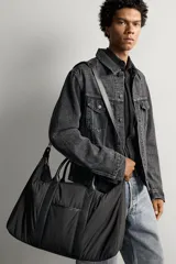 Bolso de viaje tipo bowling fabricado en combinación de nylon y detalles en cuero sintético, de color negro. Cuenta con compartimento principal con cierre de cremallera, bolsillo frontal plano, dos asas de mano y un asa de hombro ajustable y extraíble.