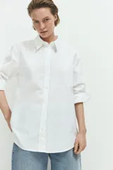Camisa blanca de corte relajado, cuello clásico, mangas largas y cierre frontal con botones.