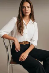 Blusa blanca oversize de poliéster, con cuello camisero, mangas 3/4 abullonadas y cierre frontal con botones.