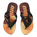 Ojotas (chancletas) con estampa de atardecer tropical en tonos naranjas, amarillos y marrones. Tienen tiras negras con el logo de Mormaii en naranja en una de ellas.